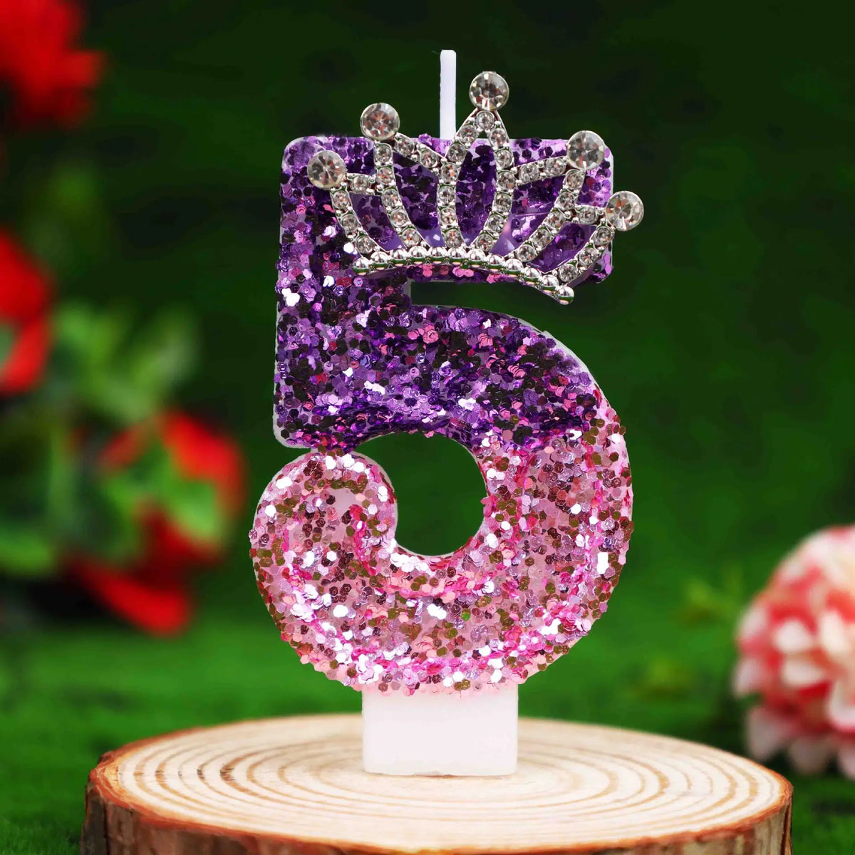 A glitter number 5 birthday candle with a rhinestone crown cake topper on a wooden surface.