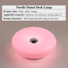 Pinke, donutförmige Schreibtischlampe mit Lichtschein, die Design und Beleuchtung zeigt.