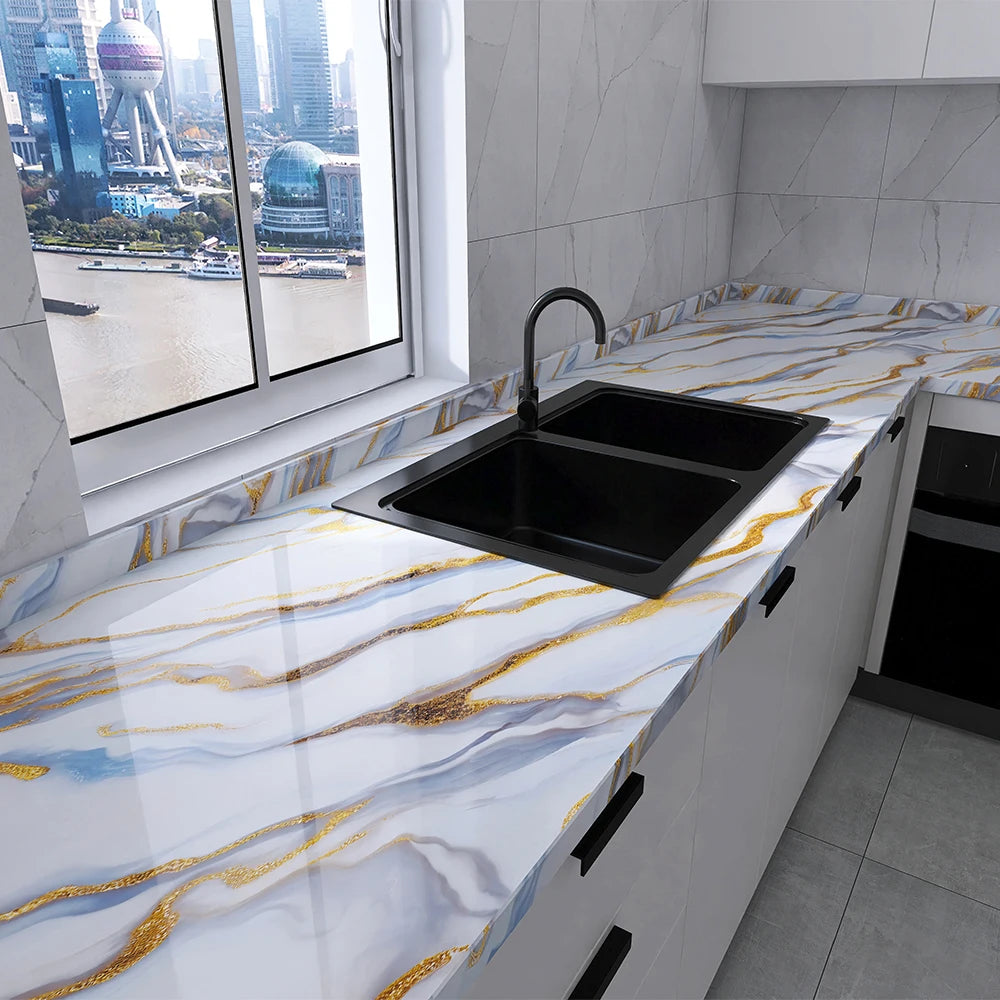 A modern kitchen countertop with a black sink and white marble featuring gold veining, set against a window view of a city sk