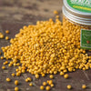 A pile of yellow granular slow-release plant fertilizer is shown next to a jar.