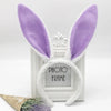 A pair of purple bunny ear headbands displayed in a white photo frame.