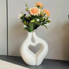A bouquet of peach and orange roses and white filler flowers displayed in a modern, white heart-shaped vase.