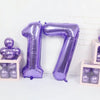 A purple foil number balloon shaped like the number 17 stands next to small boxes filled with purple balloons.