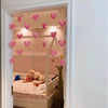 A heart-shaped string door curtain with romantic bead design hangs in a doorway, illuminating a bedroom interior.