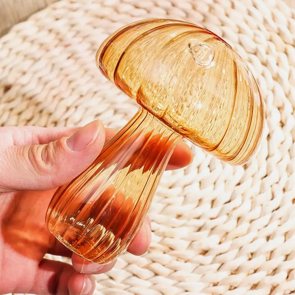 A hand holds a translucent, mushroom-shaped glass vase with swirling amber and reddish tones against a woven background.