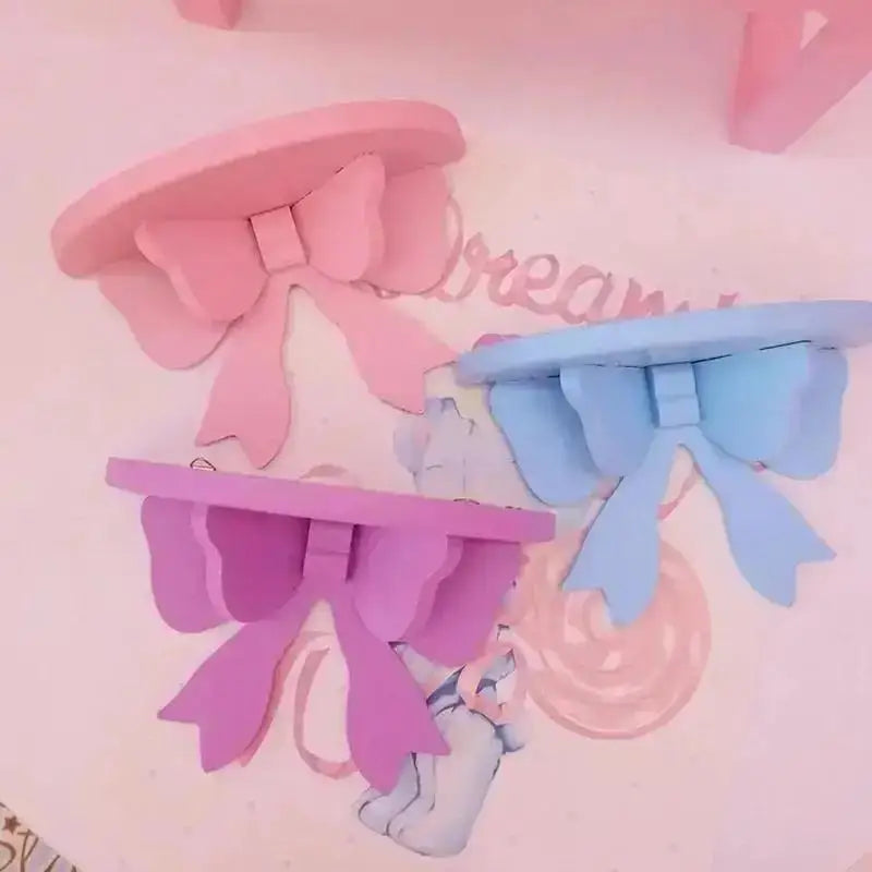 Pink and blue decorative bow-shaped wooden wall shelves displayed on a light pink background.