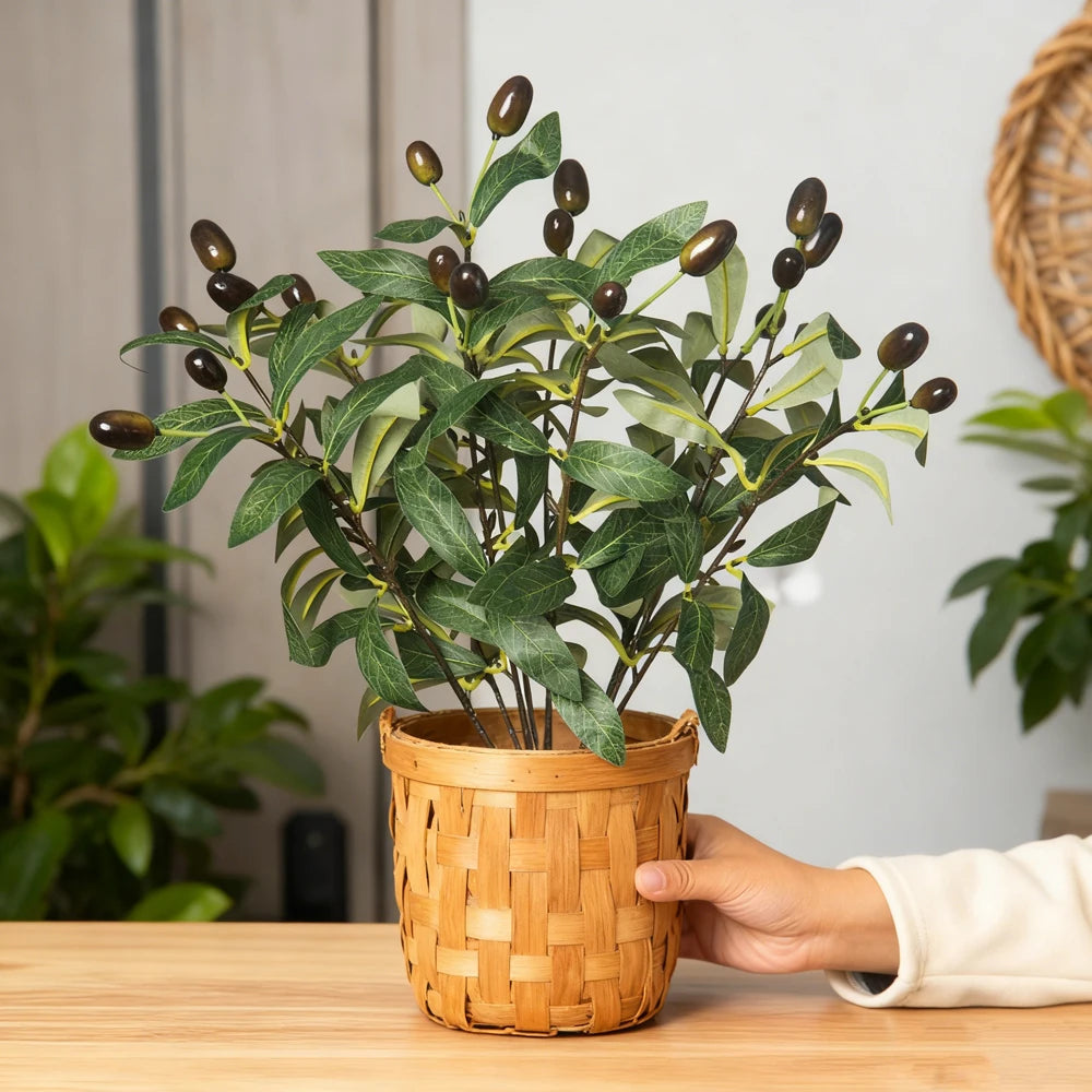 Artificial olive tree branch with green leaves and dark berries potted in a woven basket