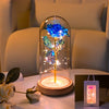 An LED galaxy rose artificial flower displayed inside a glass dome on a white surface.