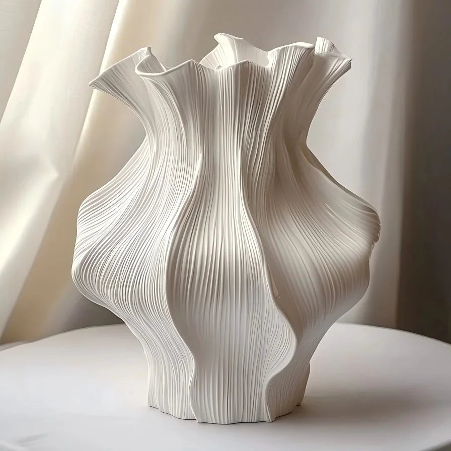A white ceramic vase with vertical wave patterns is displayed on a light surface.