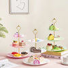 A three-tier plastic cupcake stand displaying various decorated cupcakes and pastries on a pink table.