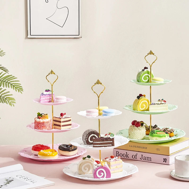 A three-tier plastic cupcake stand displaying various decorated cupcakes and pastries on a pink table.
