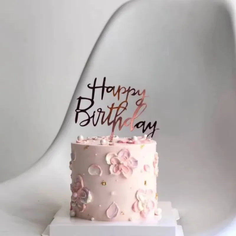A pink birthday cake decorated with floral accents and gold details, set against a light background.