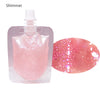 A pink lip oil gloss product in a clear plastic container and a circular swatch showing glitter texture.