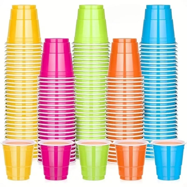 A collection of colorful disposable plastic shot cups in yellow, pink, green, and blue stacked vertically.