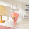 A clear plastic bag contains a handmade crochet flower bouquet with pink and yellow flowers tied with a pink ribbon.