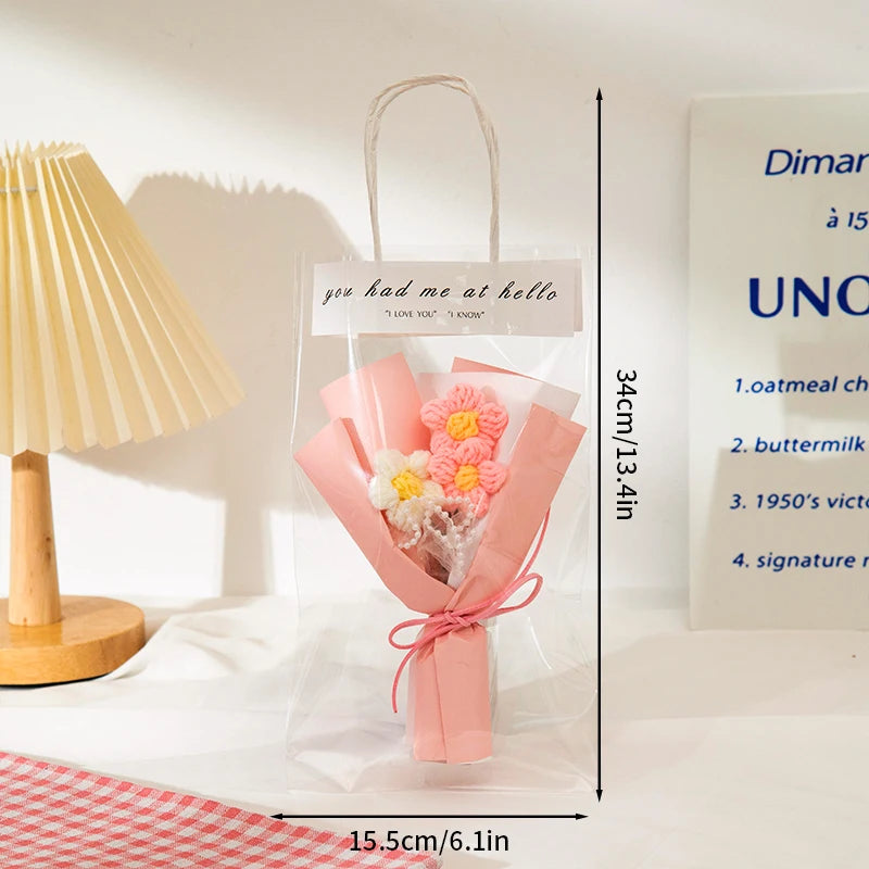 A clear plastic bag contains a handmade crochet flower bouquet with pink and yellow flowers tied with a pink ribbon.