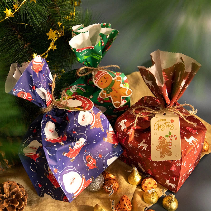 A festive arrangement of Christmas kraft paper gift bags tied with twine and seal stickers on a gold-colored surface.