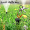 A close-up of a black key hider inserted into green grass, with a key visible above it.