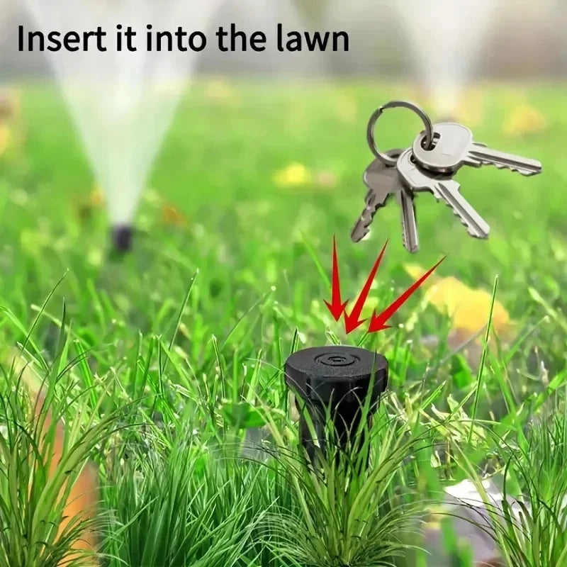 A close-up of a black key hider inserted into green grass, with a key visible above it.