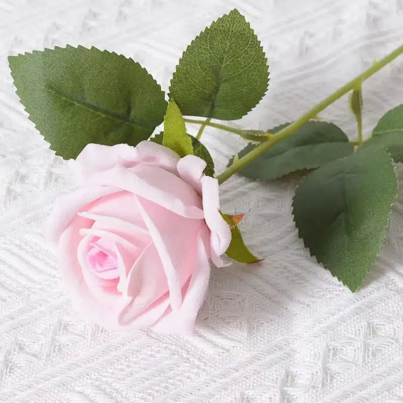 A pink velvet artificial rose with green leaves on a stem, used for weddings and home decor.