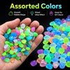 A hand holds assorted glow-in-the-dark luminous pebbles in various colors like blue, green, and pink.