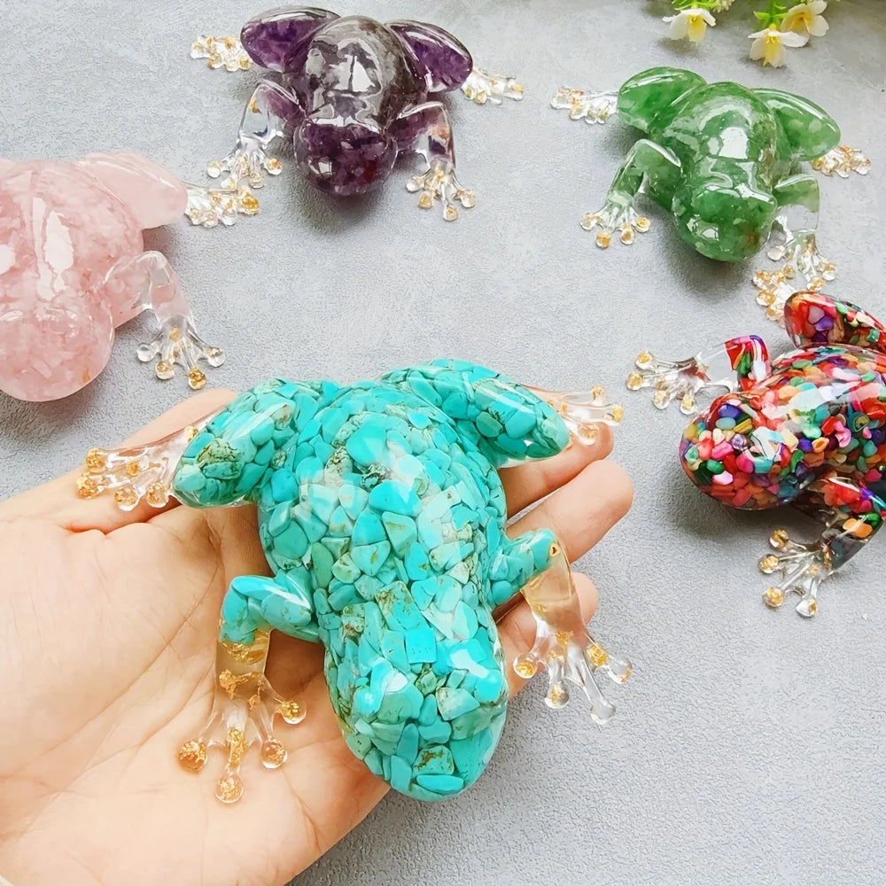 A hand holds a bright turquoise crystal frog resin craft decoration surrounded by other colored frogs.