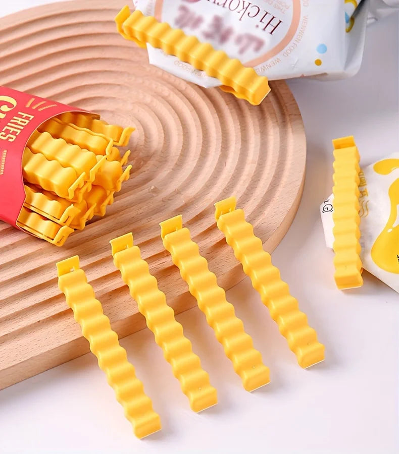 A collection of yellow, fry-shaped sealing clips is displayed on a wooden board next to a package of fries.