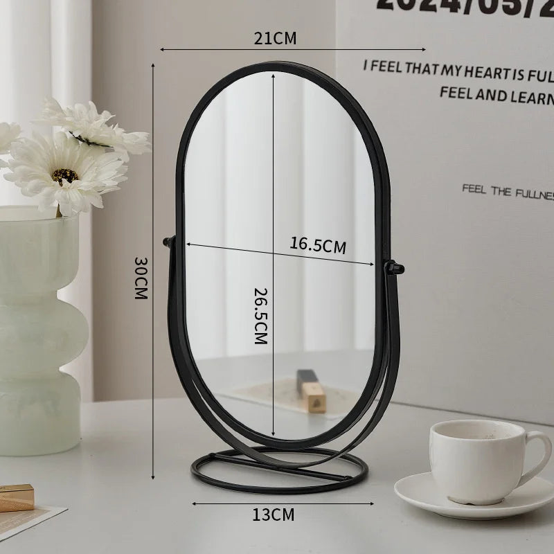 A black oval vanity mirror with a white frame and stand is shown on a table.