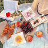 A flat lay of pastries, bread, and swiss rolls arranged in minimalist kraft boxes on a striped cloth.