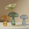 Three mushroom-shaped glass vases in translucent jelly colors arranged on a white surface with a sprig of baby's breath.
