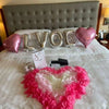 Pink artificial silk rose petals arranged in a heart shape on a white bed.