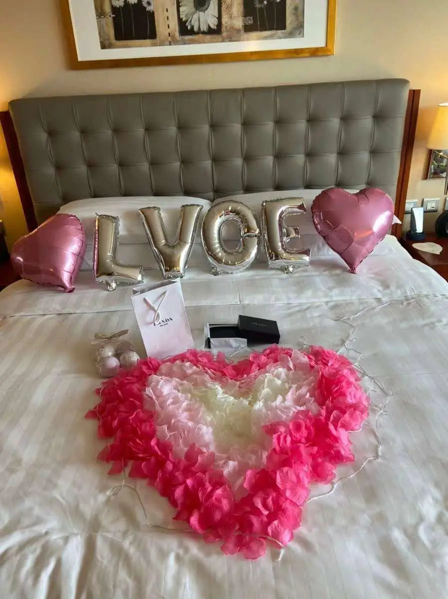 Pink artificial silk rose petals arranged in a heart shape on a white bed.