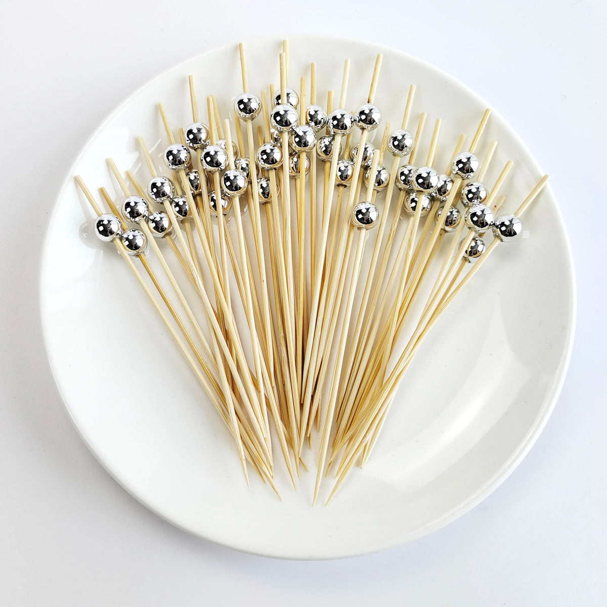 A plate holds numerous bamboo cocktail picks with pearl-tipped metal decorations.
