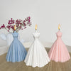 A white and pink silicone mold of a wedding dress is displayed with lit candles on a wooden surface.