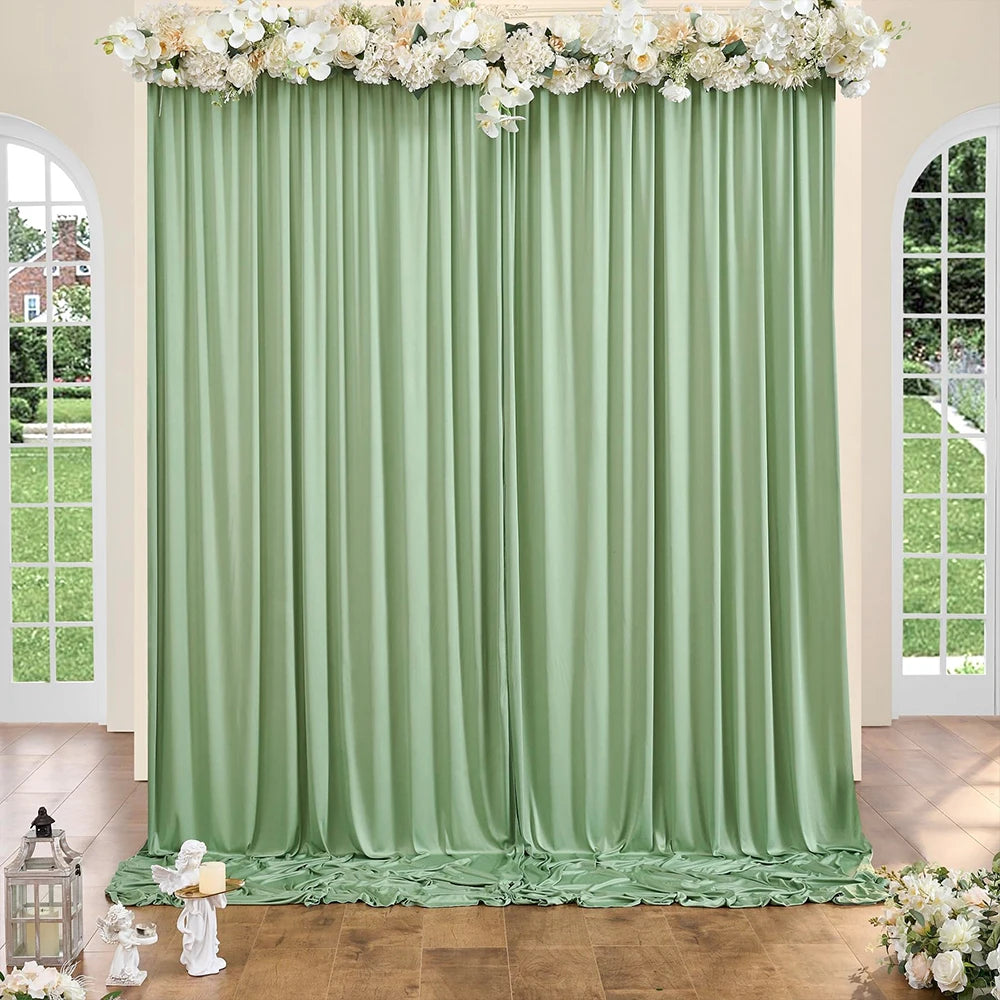 A floor-to-ceiling light sage green fabric backdrop with white floral garlands and antique lanterns.