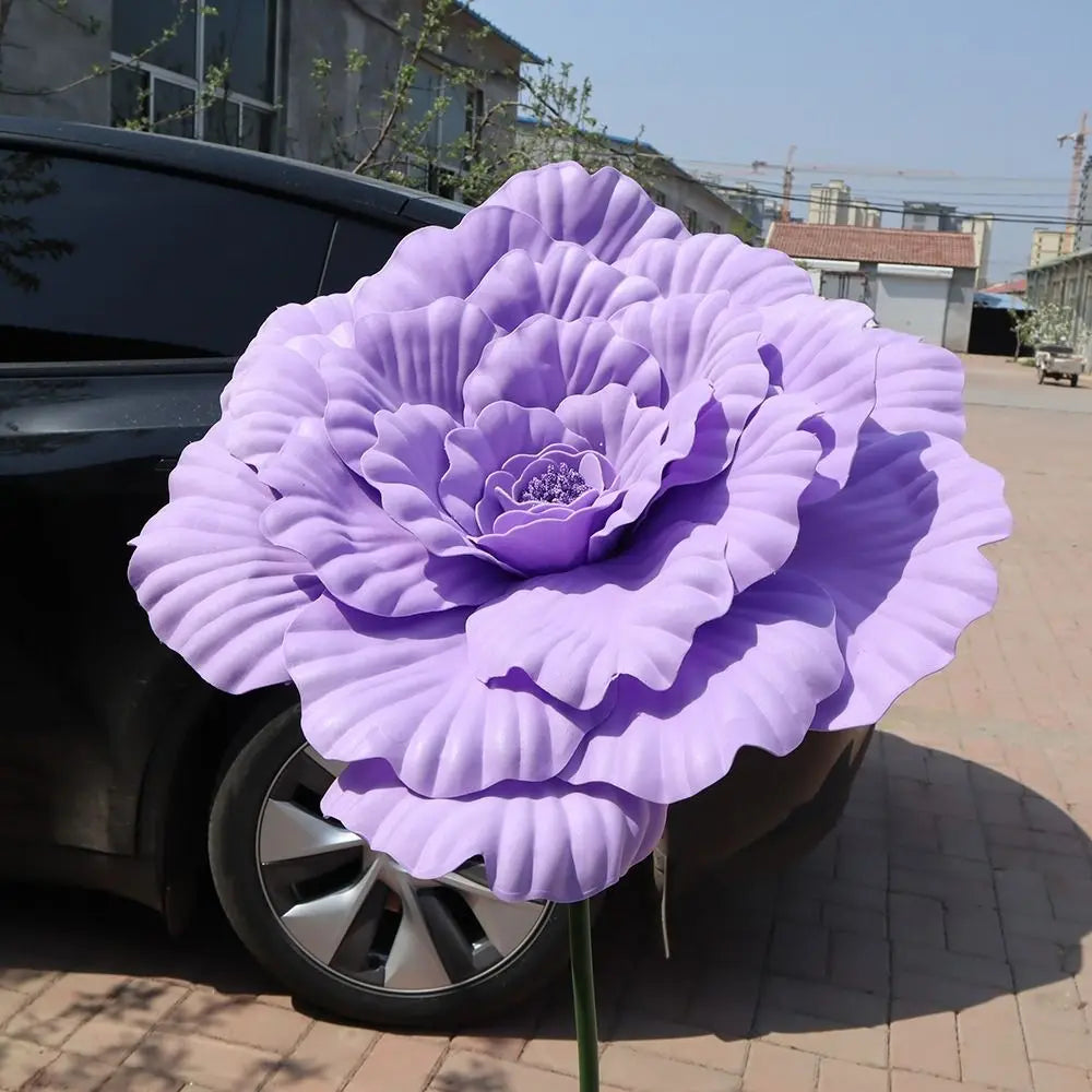 A large, purple artificial peony flower is displayed on a car wheel.