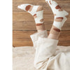 A pair of beige plush socks with brown cat paw prints are shown resting on a light-colored rug.