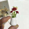 A hand holds a white ceramic vase with artificial red and white flowers, used as a fridge magnet.