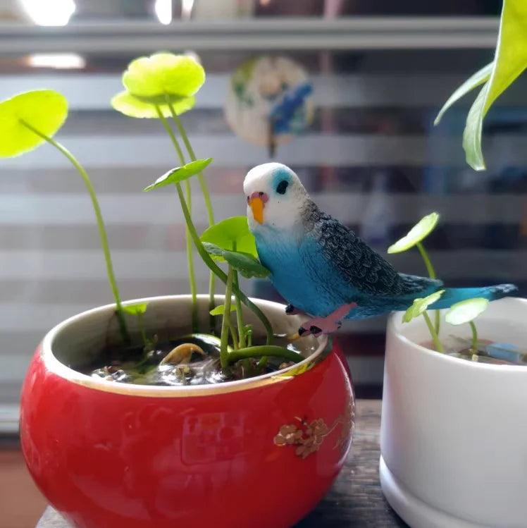 A blue and white pet bird figurine with green leaves is placed in a red bowl, set against a blurred background.