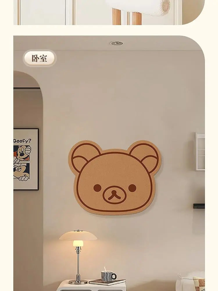 A round, brown cartoon bear felt wall decor panel hanging on a light beige wall above a table lamp.