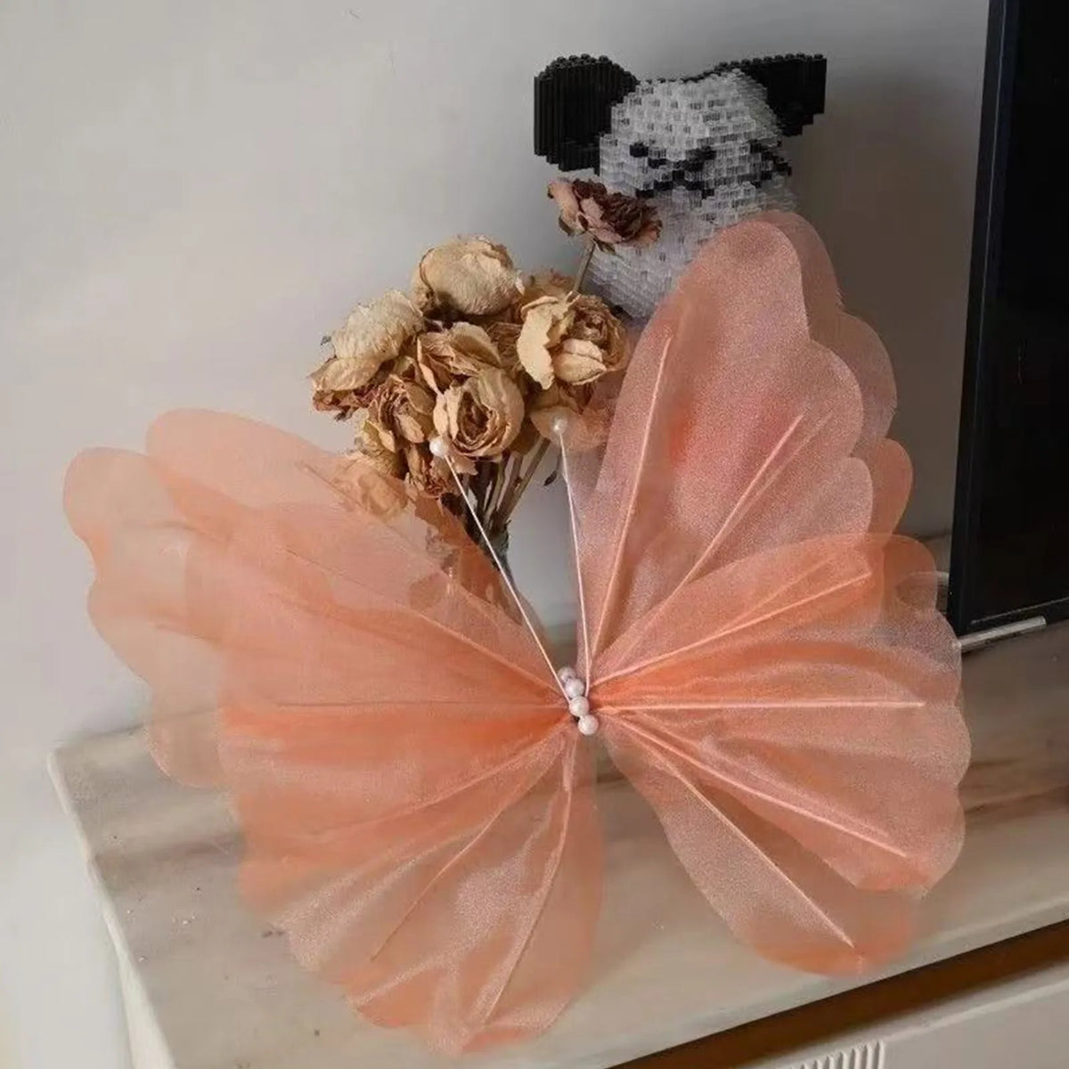 A delicate peach colored mesh butterfly decoration with a black and white textured animal head attached.