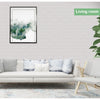 A living room decorated with a white sofa, light rug, and a framed watercolor painting of misty green landscape.