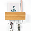 A light wood bamboo wall-mounted key rack with six metal hooks and a pink wooden stick.