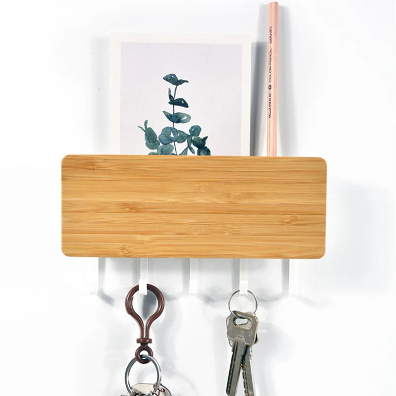 A light wood bamboo wall-mounted key rack with six metal hooks and a pink wooden stick.
