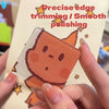 A hand holds a square, translucent orange-toned fridge magnet with precise edge trimming and smoothing.