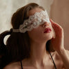 A woman wearing an elegant white lace masquerade eye mask, looking upwards.