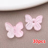 Un juego de 30 cuentas de mariposa de vidrio rosa sobre una superficie gris texturizada.