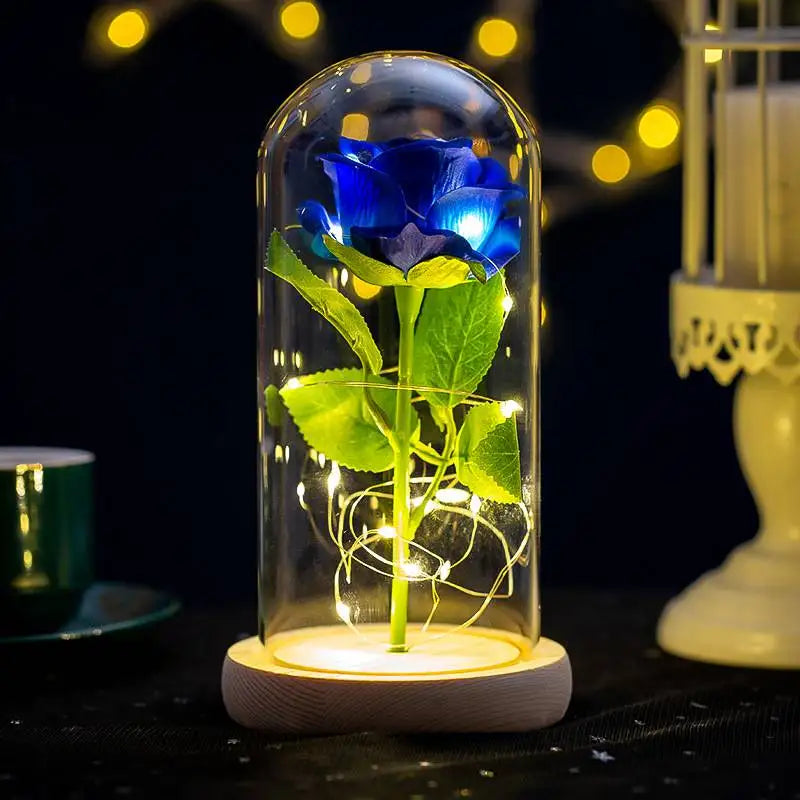 A glass enclosure displays a realistic blue rose with green leaves, illuminated by internal LED lights.
