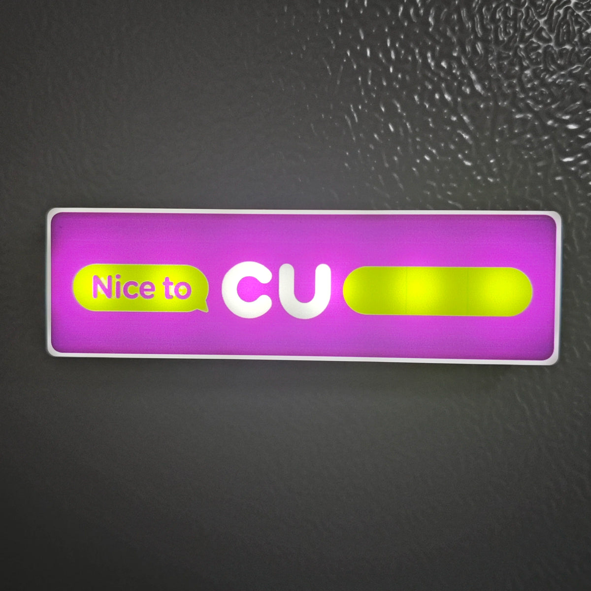A rectangular sign with purple background featuring the text Nice to CU in yellow and white.
