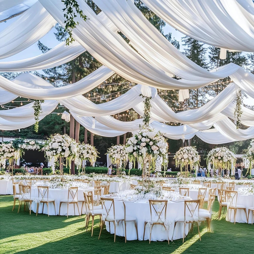 Elegant white fabric drapery and floral arrangements creating a romantic outdoor event backdrop.